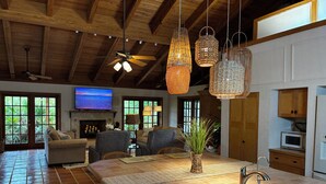 A spacious living area with a large TV, comfortable seating, a kitchen with a sink, and a ceiling fan.