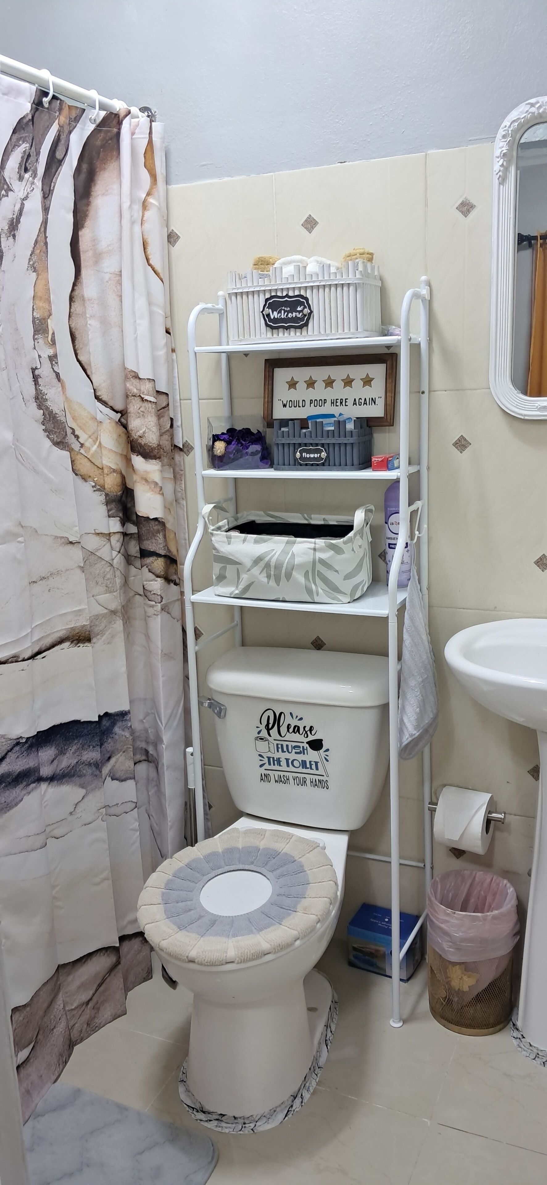 Un baño con inodoro, un estante con artículos de aseo, lavamanos y cortina de ducha.