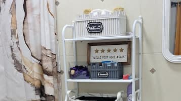 Un baño con inodoro, un estante con artículos de aseo, lavamanos y cortina de ducha.