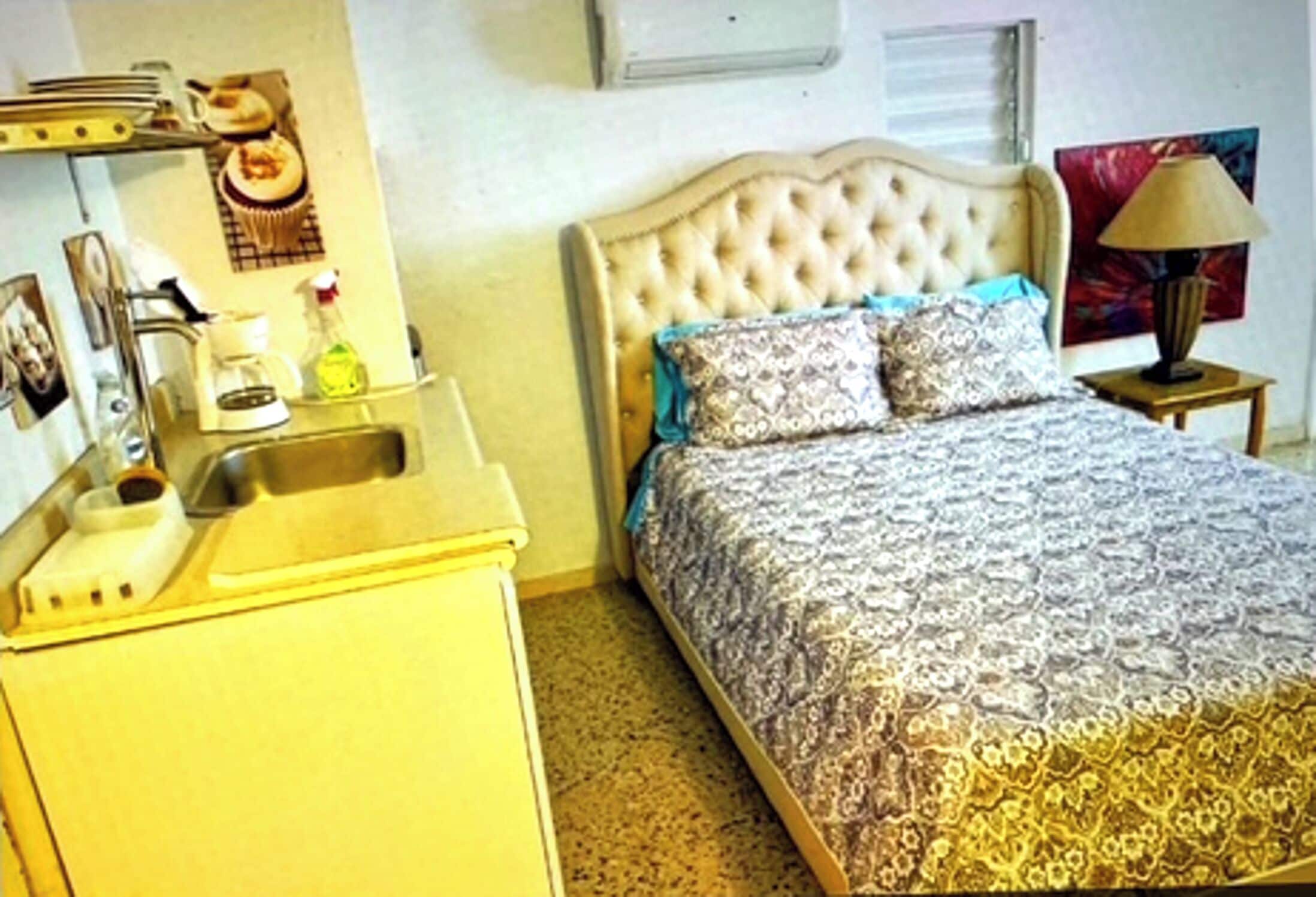 A bedroom with a bed, a bedside table, a lamp, a mirror, and a dresser.
