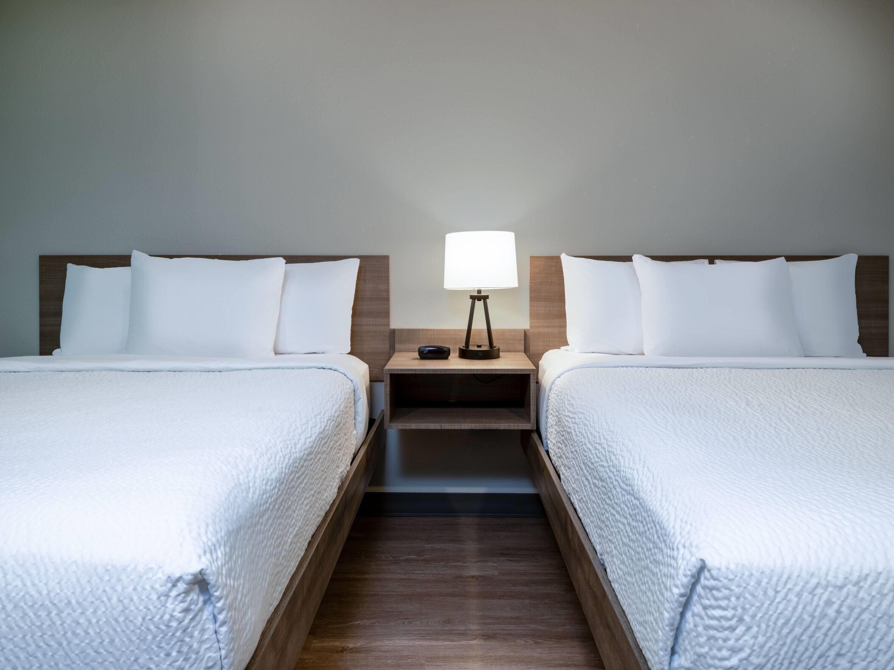 A hotel room with two beds, a nightstand with a lamp, and a wooden floor.