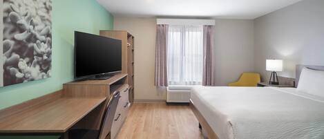 A hotel room with a bed, desk, chair, television, and a window with curtains.