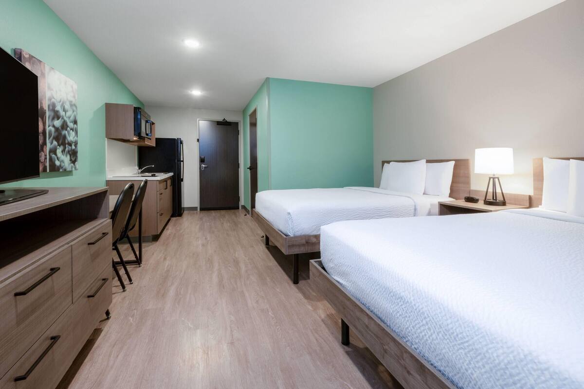A hotel room with two beds, a desk, a television, and a door leading to a bathroom.