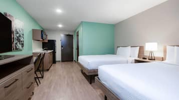 A hotel room with two beds, a desk, a television, and a door leading to a bathroom.