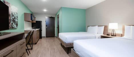 A hotel room with two beds, a desk, a television, and a door leading to a bathroom.