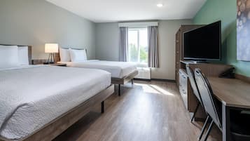 A hotel room with two beds, a desk, a chair, a TV, and a window with curtains.