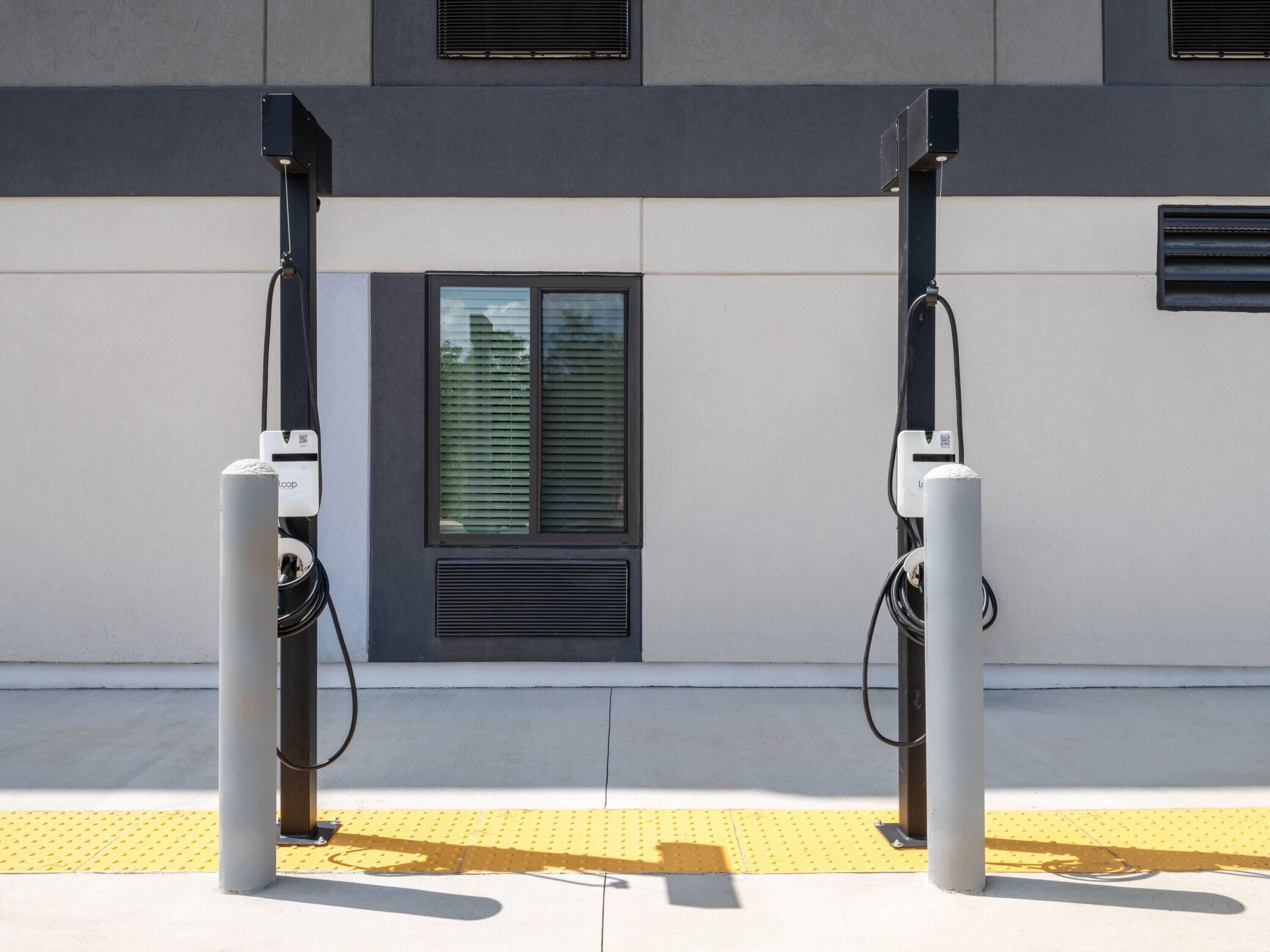 Two electric vehicle charging stations mounted on a building facade with a window and ventilation grilles.