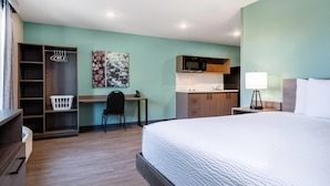 Een hotelkamer met een bed, een bureau, een stoel, een kledingkast, een magnetron, een wastafel en een lamp.