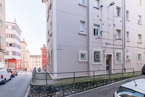 A multi-story residential building with balconies, a stone wall, and a metal railing along the street.
