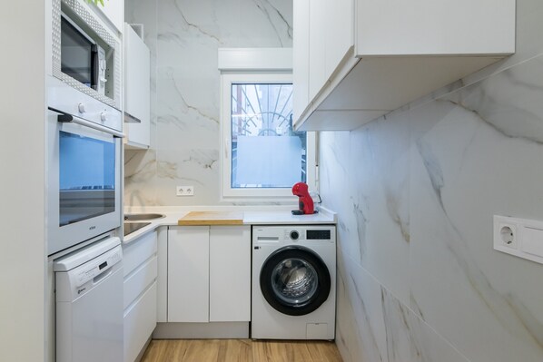 A compact kitchen with a washing machine, a microwave, and a window.