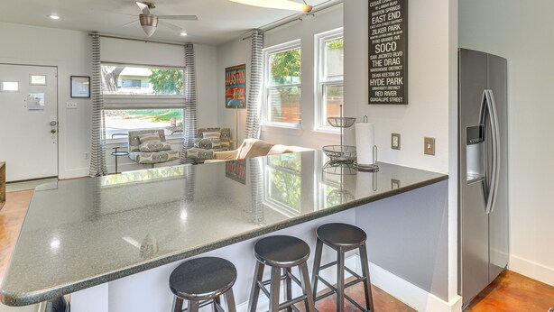 A modern kitchen with a large island, bar stools, a refrigerator, and a view of the outdoors. - Cowboy Pool & Balcony: Home 1 Mi to Dtwn Austin! (Austin)