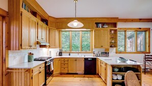 Une cuisine avec des meubles de rangement en bois, une cuisinière, un évier et une fenêtre donnant sur les arbres.