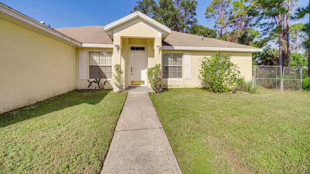 A single-story house with a front entrance, a small front yard, and a chain-link fence. - Spacious Palm Bay Stay! Family Home Near Beaches (Palm Bay)