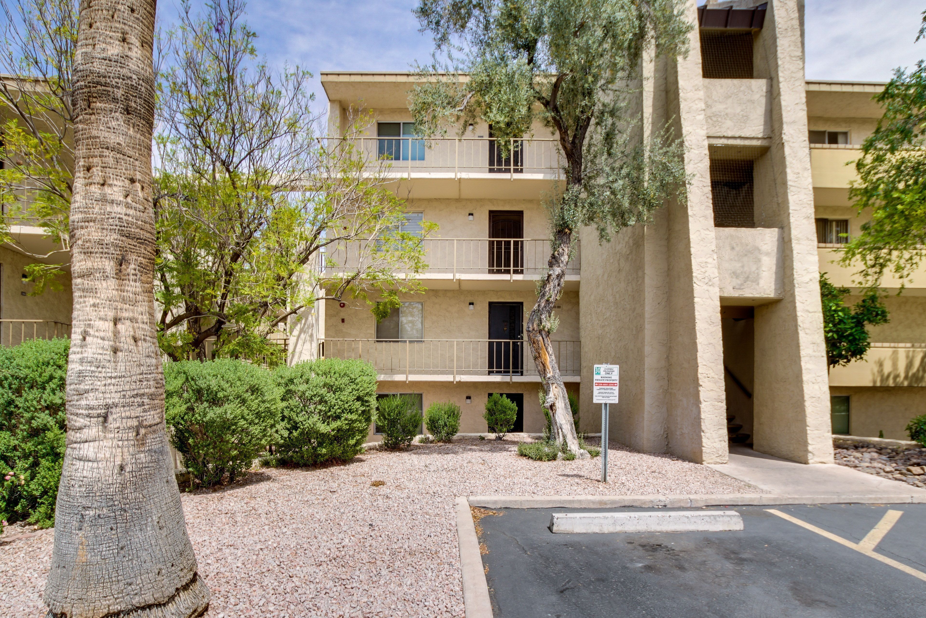 A multi-story building with balconies, surrounded by trees and shrubs.