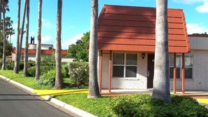 A small, single-story building with a red roof, surrounded by palm trees and a well-maintained lawn. - Pleasant corporate apartment with AC in Donna (Donna)