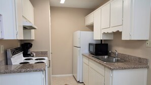 A compact kitchen with white cabinets, a stove, a refrigerator, and a microwave. - Pleasant corporate apartment with AC in Donna (Donna)