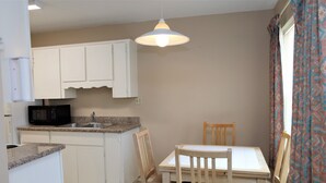A compact kitchen with white cabinets, a microwave, and a dining table with chairs. - Pleasant corporate apartment with AC in Donna (Donna)