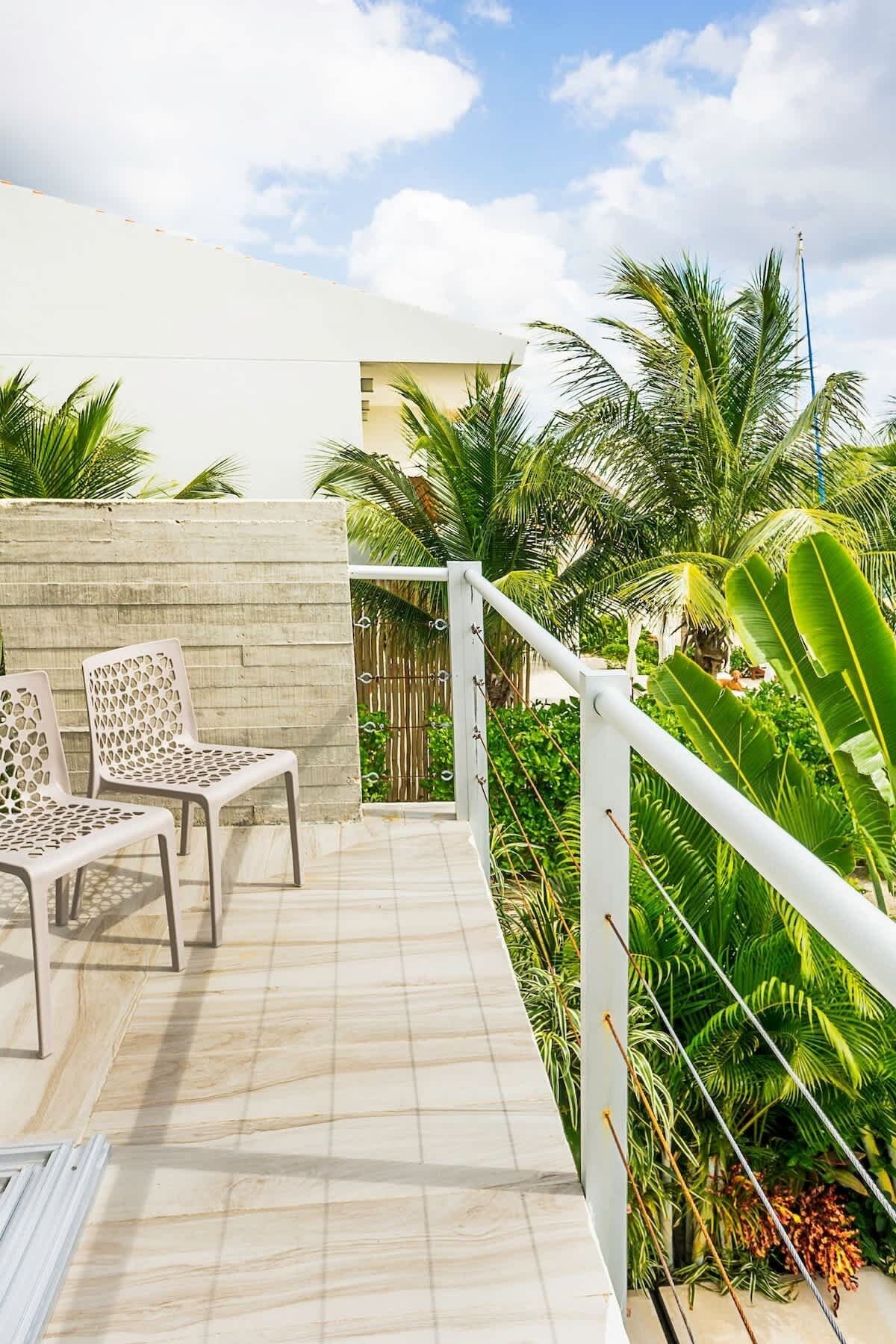 Une terrasse avec deux chaises blanches, un sol carrelé et une végétation tropicale luxuriante.