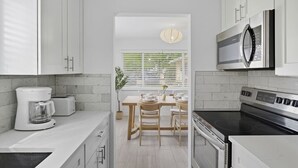 Une cuisine moderne avec des meubles blancs, un four à micro-ondes encastré, une cuisinière et une machine à café. Il y a également un coin repas avec une table et des chaises.
