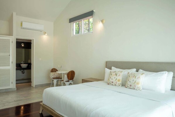 Ein Schlafzimmer mit einem Bett, einem kleinen Tisch, zwei Stühlen, einem Fenster und einer Klimaanlage.