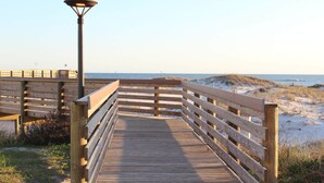 Une promenade en bois menant à une plage, avec un lampadaire et une vue lointaine sur l’océan.