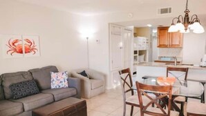 A living room with a sofa, a coffee table, and a dining area with chairs and a table. - Plantation Palms 6108 (Baldwin County)