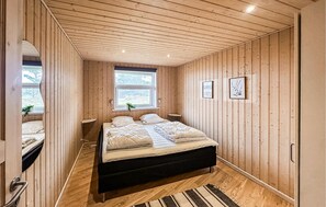 A bedroom with a bed, a window, a bedside table, and a wall-mounted picture.
