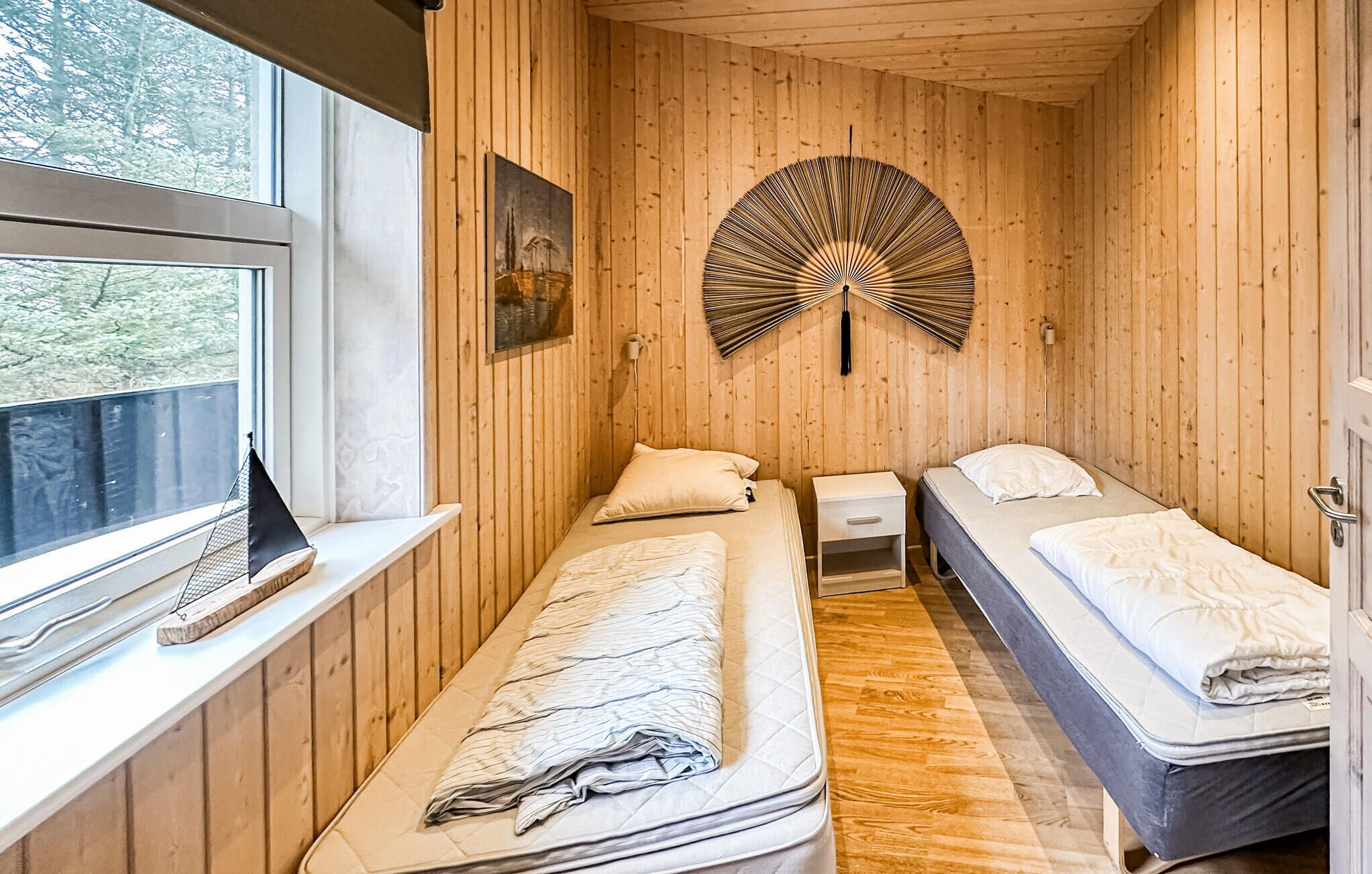 Une petite pièce chaleureuse aux murs en bois, avec deux lits, une fenêtre et une décoration murale originale.