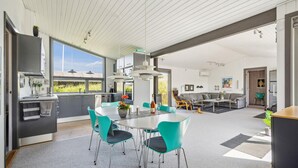 A modern kitchen with a dining area, large windows, and a view of greenery.