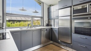 A modern kitchen with stainless steel appliances, grey cabinetry, and a large window offering a view of greenery.