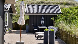 A patio with a table and chairs, a white umbrella, and planters with plants.