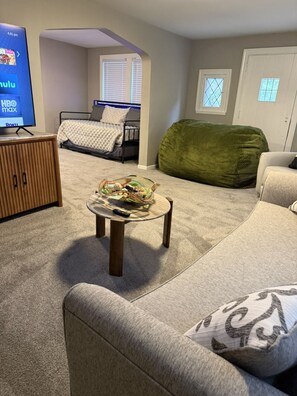 Ett mysigt vardagsrum med en soffa, ett soffbord med snacks, en tv-skärm som visar HBO Max och en säng i bakgrunden.