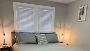A bedroom with a large bed, two bedside tables, a window with blinds, and a framed picture on the wall. - Perfect for Families, newly remodeled (Glendale)