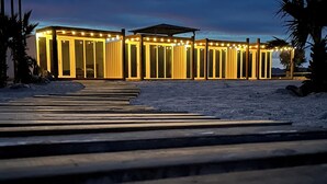 En modern byggnad med en rad upplysta dörrar och ett takförsett utomhusområde dekorerat med ljusslingor.