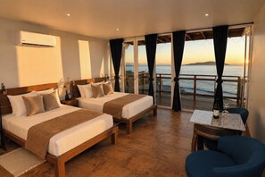 Ein Hotelzimmer mit zwei Betten, einem kleinen Tisch mit einer Flasche und Gläsern, einem Stuhl und Blick aufs Meer.