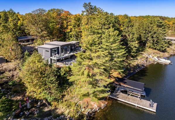 Ein modernes Haus mit Terrasse, das auf einen See mit Blick auf dichten Wald blickt.
