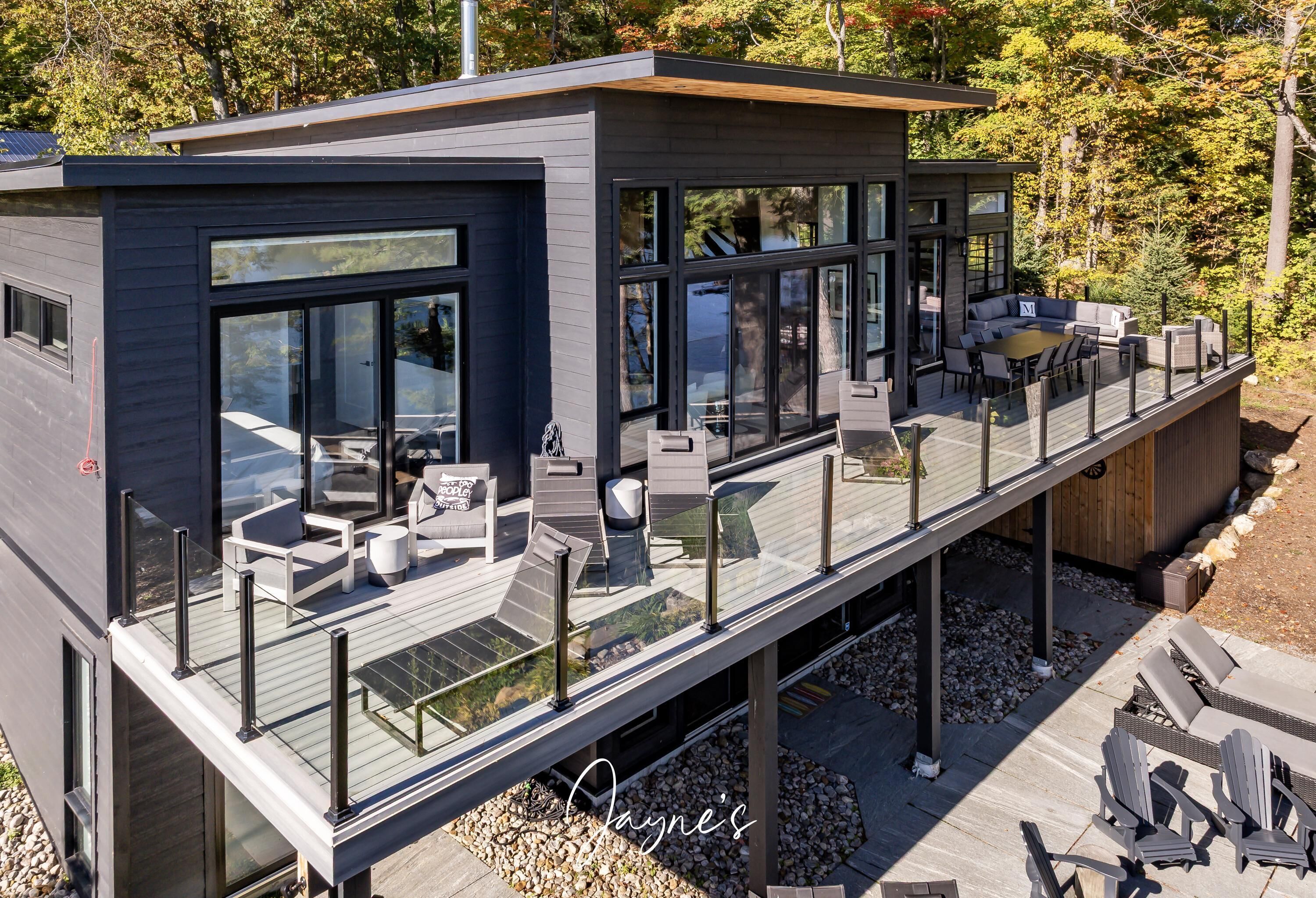 A modern house with a deck, outdoor seating, and a view of trees.