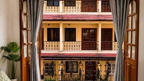 Habitación de hotel con una cama, dos toallas enrolladas, una planta en maceta y vistas a un edificio con balcones.
