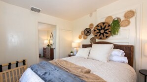 Een slaapkamer met een groot bed, een houten ledikant en een wand versierd met geweven manden en een hangplant.