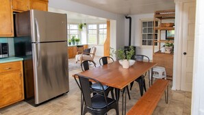 Een moderne keuken met een roestvrijstalen koelkast, houten kasten, een eettafel met stoelen en een kleine witte kruk.