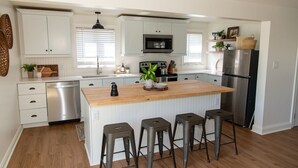 A modern kitchen with white cabinets, stainless steel appliances, a wooden island with bar stools, and a dishwasher. - Amish Cottage, Hot Tub, on Mill Creek (Lancaster)
