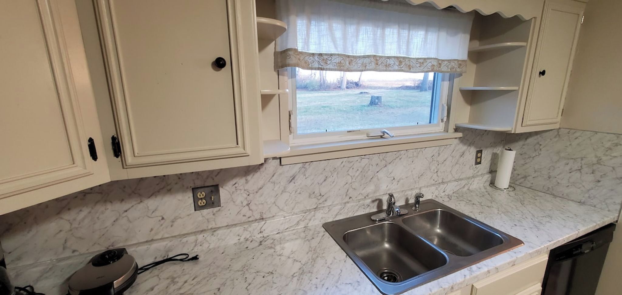 Una cocina con encimeras de mármol, un lavamanos doble y una ventana con vista a una zona verde.