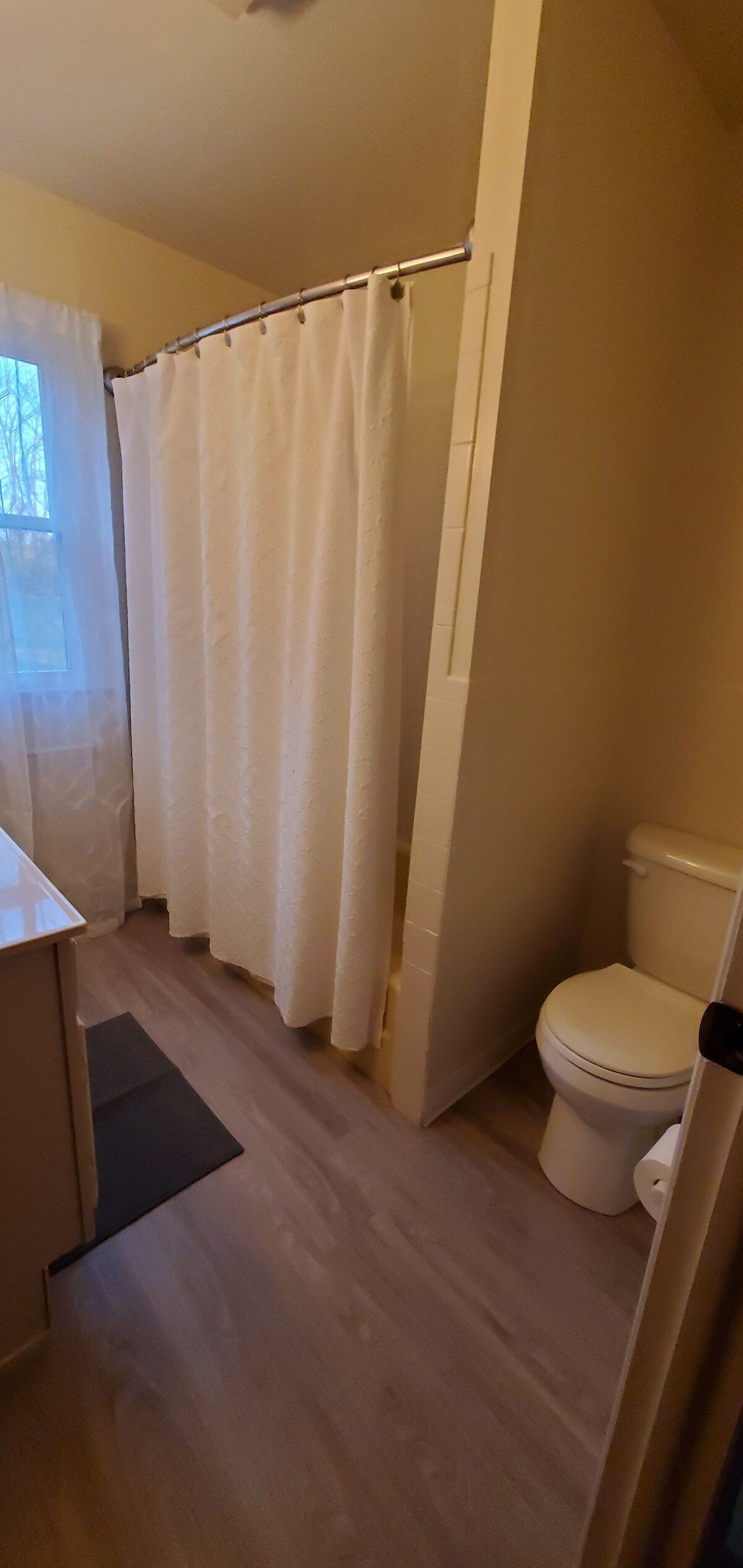Un baño con cortina de ducha, inodoro y una alfombra pequeña en el suelo.