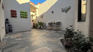 Un patio con piso de piedra, una zona de estar con mesa y sillas, y decoración mural.