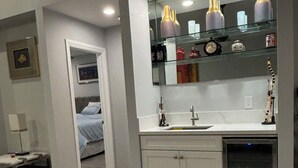 Una cocina moderna con lavavajillas integrado, un armario con puerta de vidrio que exhibe objetos decorativos, y un acceso a un dormitorio.