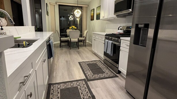 Una cocina moderna con electrodomésticos de acero inoxidable, armarios blancos y un comedor con candelabro.
