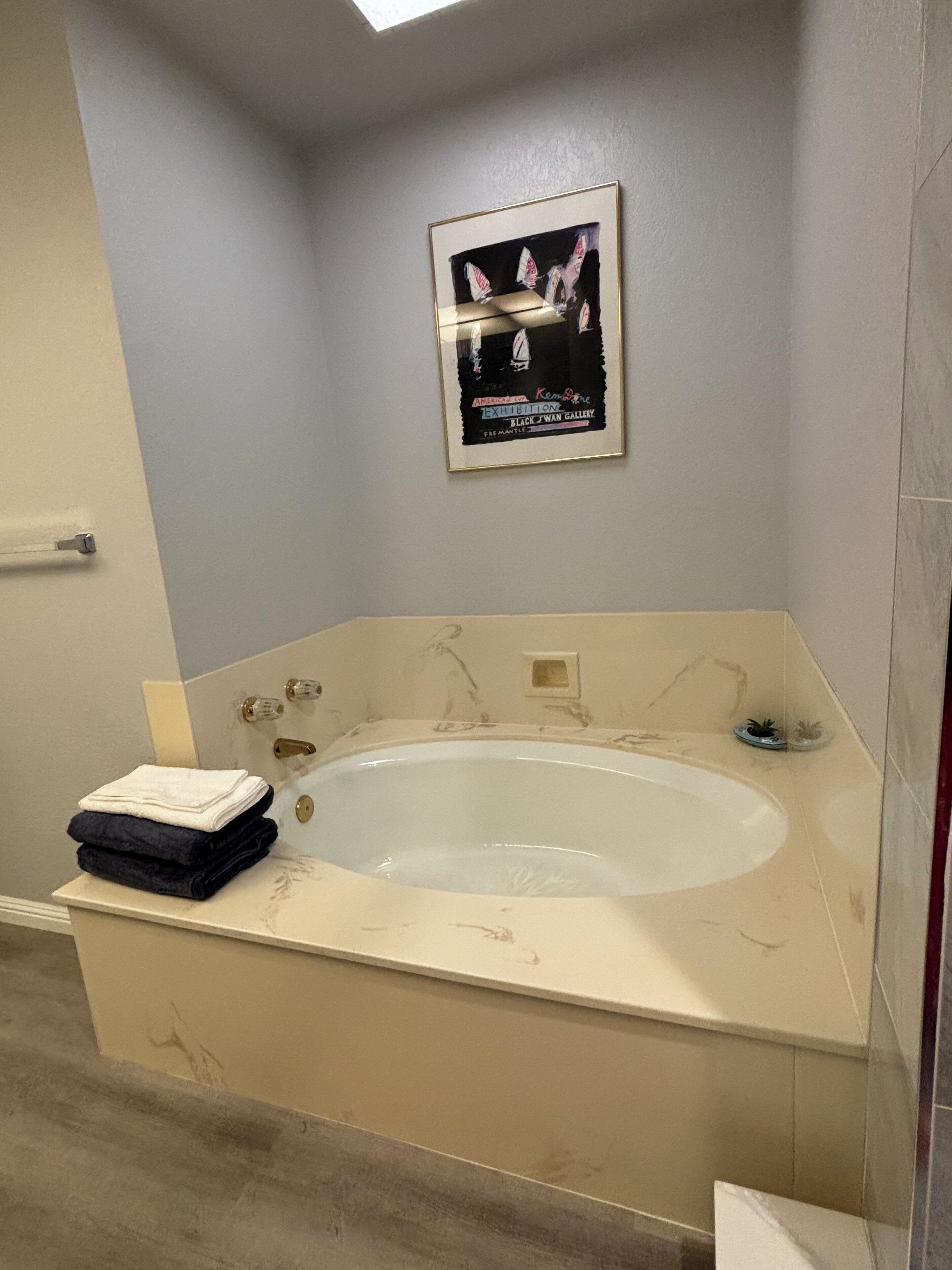 Ein Badezimmer mit einer großen Badewanne, einem Stapel Handtüchern und einem gerahmten Kunstwerk an der Wand.