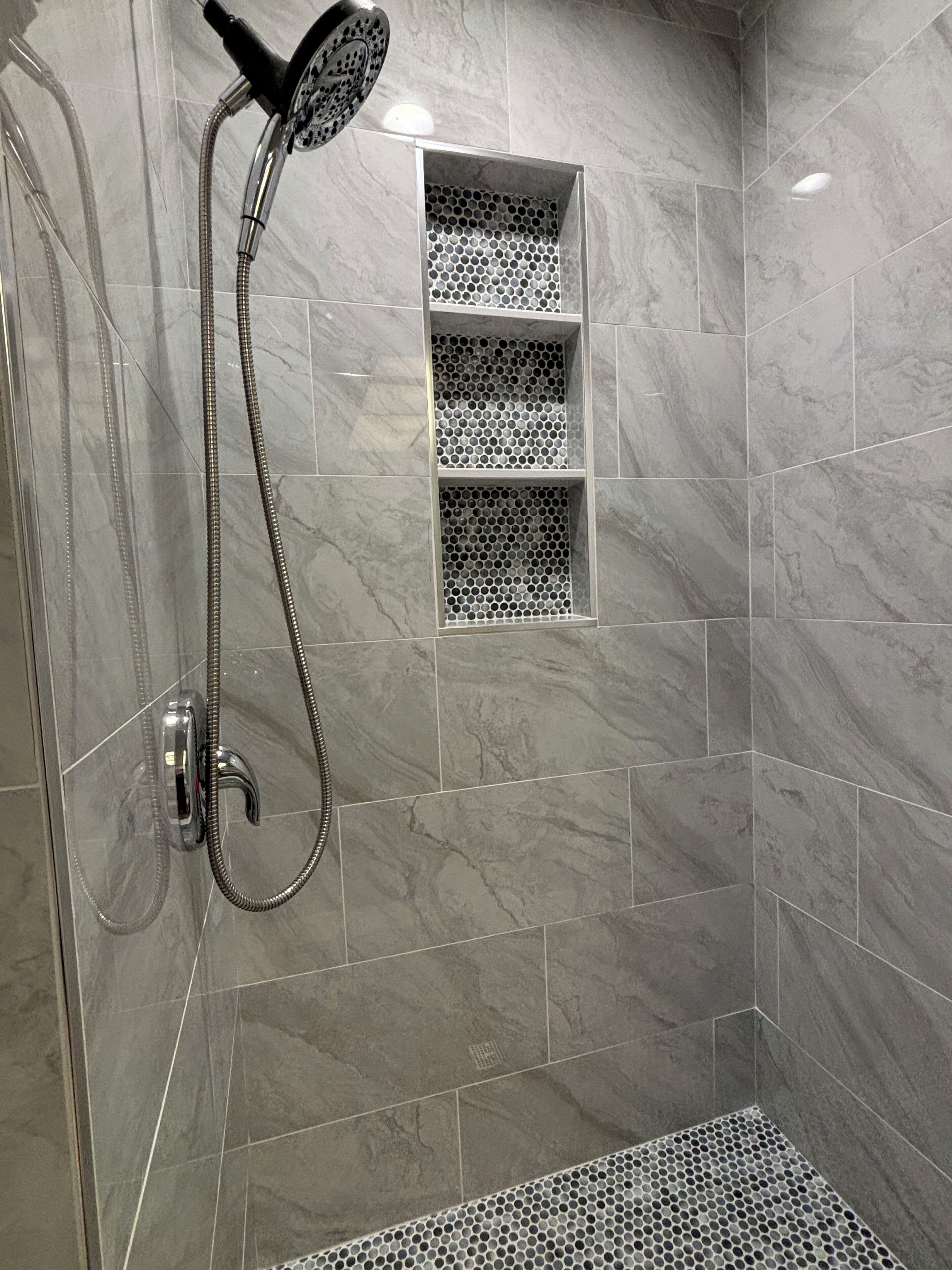Une douche équipée d’un pommeau de douche à main, d’une étagère intégrée et d’une grille d’évacuation au sol.