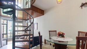 A dining area with a glass table, wooden chairs, a flower centerpiece, and a spiral staircase. - Fully Furnished Apartments in a Building With a Pool Just a few Meters From Av. Paulista Tnps (São Paulo)