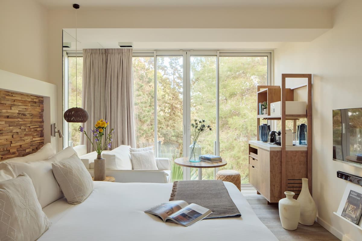 Une chambre moderne avec un grand lit, une tête de lit en bois, une petite table ornée d’un vase de fleurs et une armoire en bois avec des étagères.